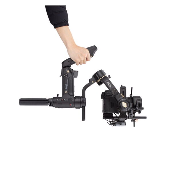 Käsi pitelee mustaa Zhiyun Crane 3S -kameravakainegimbalia, johon on asennettu kamera, vaakasuorassa valkoista taustaa vasten. Painikkeet ja kahvan yksityiskohdat näkyvät selvästi.