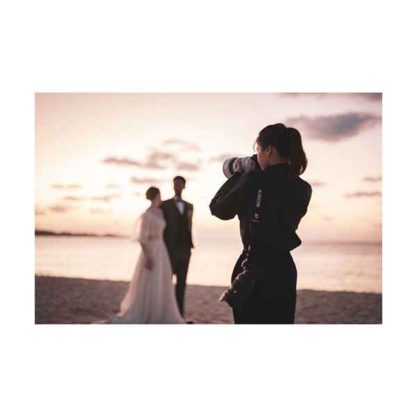 Valokuvaaja käyttää Sony FE 50-150mm f/2 GM -objektiivia ottaakseen hääkuvia morsiusparista, joka seisoo rannalla auringonlaskun aikaan, ja taustalla on meri ja elävä taivas.