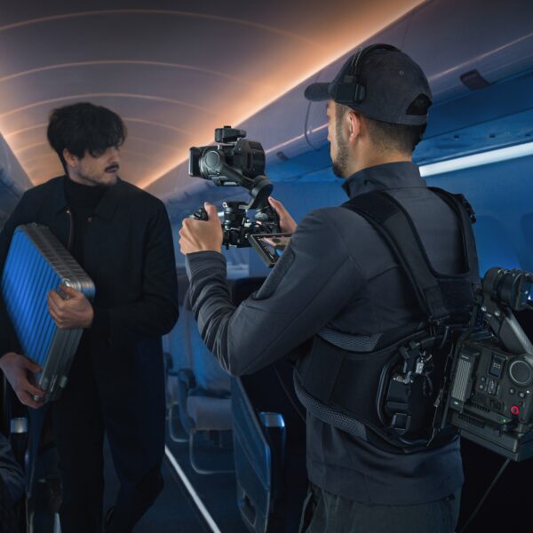 DJI Ronin 4D Flex -laitteella kuvaaja kuvaa miestä, joka kantaa sinistä matkalaukkua tyhjässä lentokoneen matkustamossa, jota valaisee sininen valaistus.