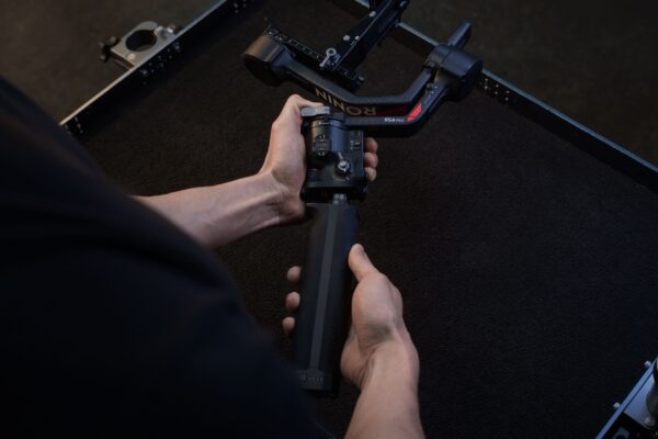 Henkilö kokoaa tai säätää DJI RS 4 Pro -käsikameragimbaalia mustalla pinnalla pitäen sen kahvasta kiinni molemmilla käsillä.